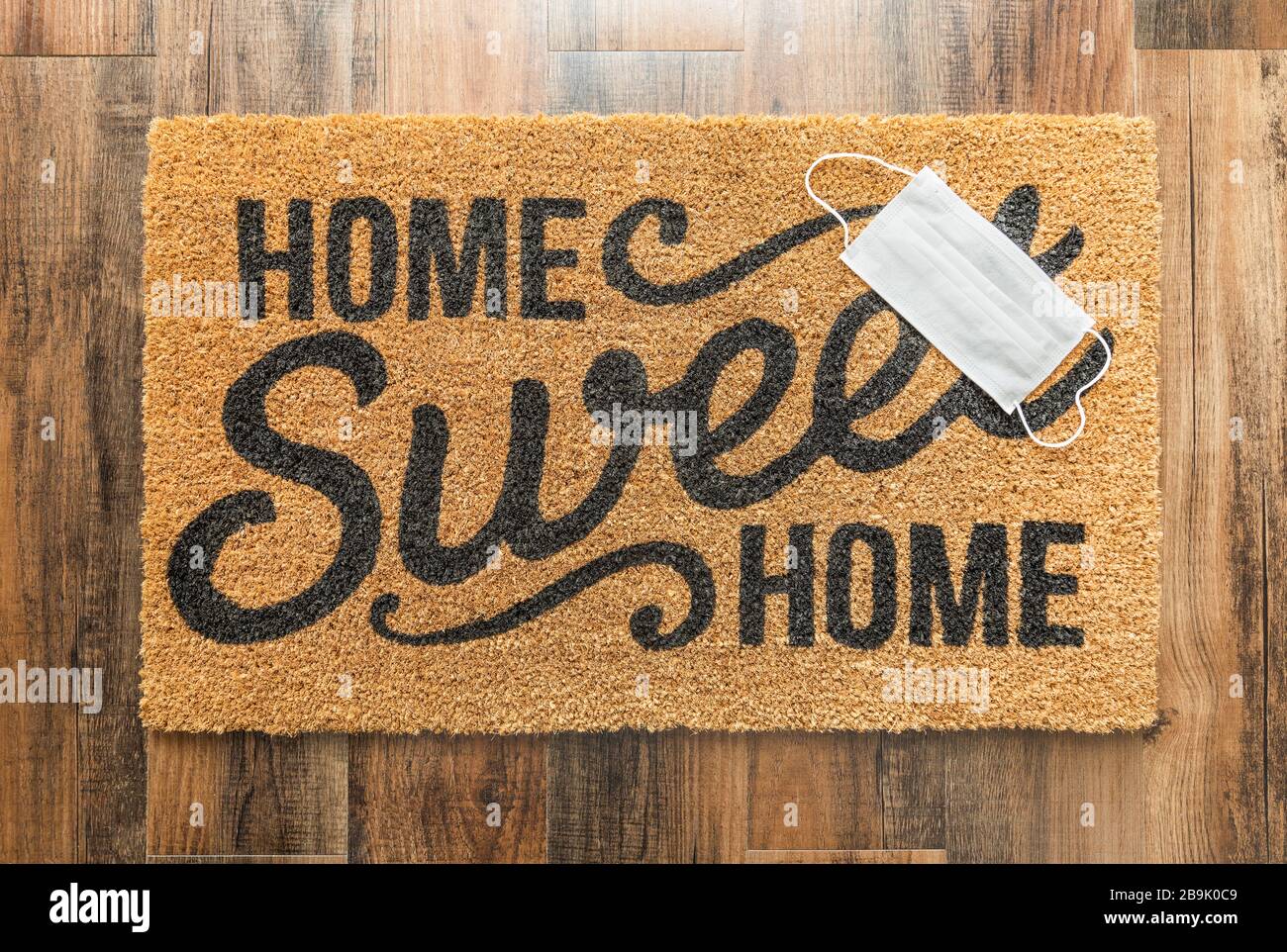 One Medical Face Mask Rests on Home Sweet Home Welcome Mat Amidst The Coronavirus Pandemic. Stock Photo