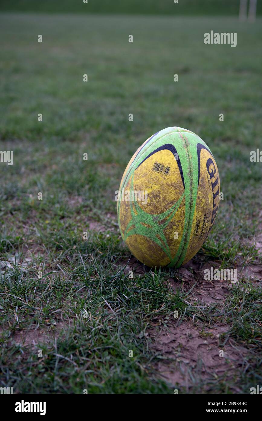 A dirty used full sized Gilbert rugby ball is placed on end in muddy field waiting to be kicked at the start of a match or for conversion after a try Stock Photo