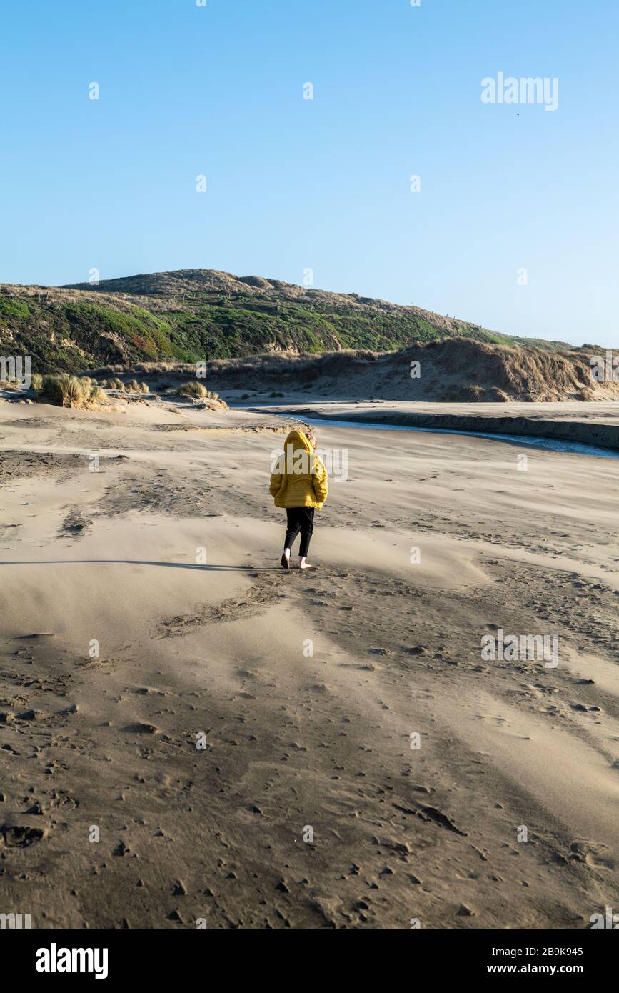 Boy walks on sandy beach tword fresh water stream leading to ocean Stock Photo