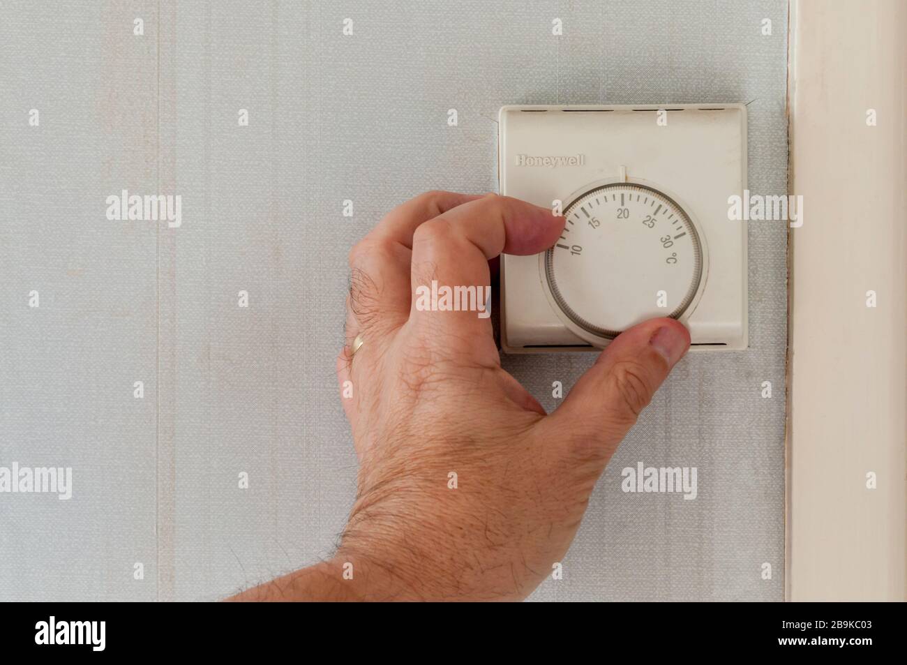 Male hand adjusting a central heating room thermostat. Stock Photo