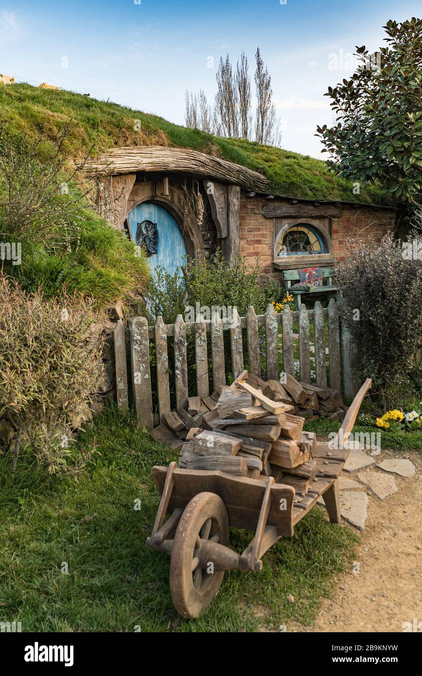 A wheelbarrow of logs outside a hobbit hole at the Hobbiton Movie Set, New Zealand Stock Photo