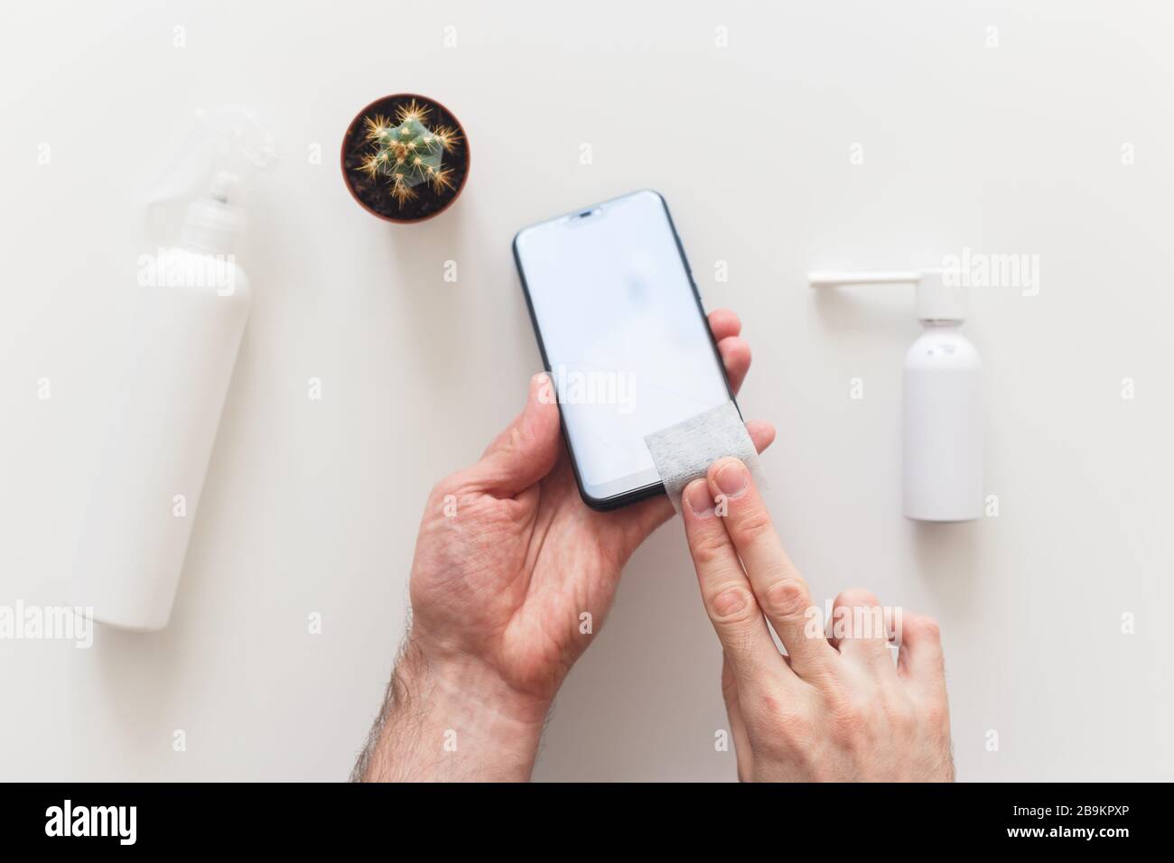 Man disinfects smartphone wiping by antibacterial wipe to prevent yourself from coronavirus COVID-19. Flat lay, on white. Stock Photo