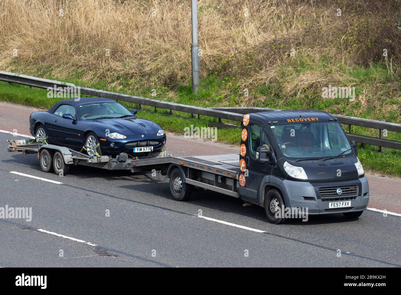 Van recovery truck carrying broken down 1999 Jaguar XKR Auto; Side view of Fiat Ducato 40 Maxi 160 M-Jet rescue breakdown recovery roadside recovery lorry truck transporter transporting, driving along  M6, Chorley UK; Vehicular traffic, transport, modern on the 3 lane highway. Stock Photo