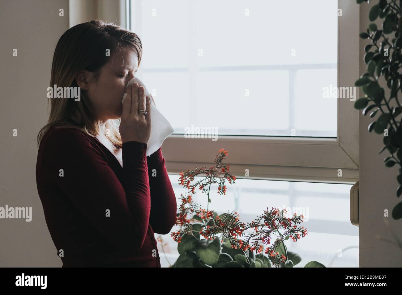 Young sick woman blowing her nose into a handkerchief by the window Stock Photo