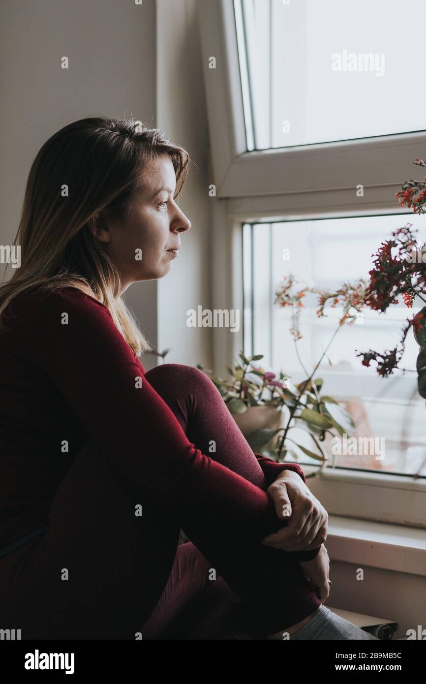 Young worried woman looking through the window Stock Photo