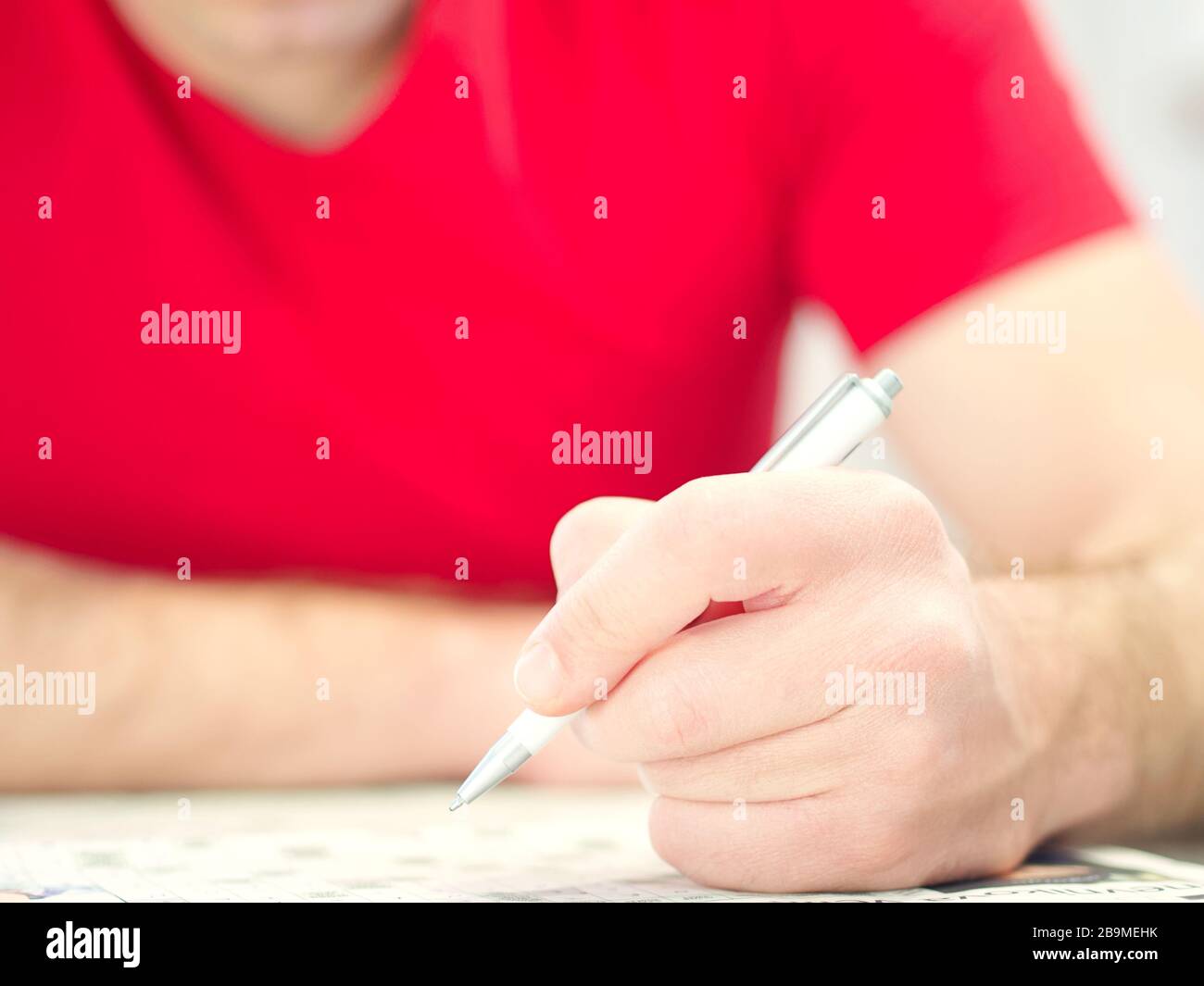 Closeup of a man hand holding a pencil solving crosswords wearing a red shirt. Stock Photo