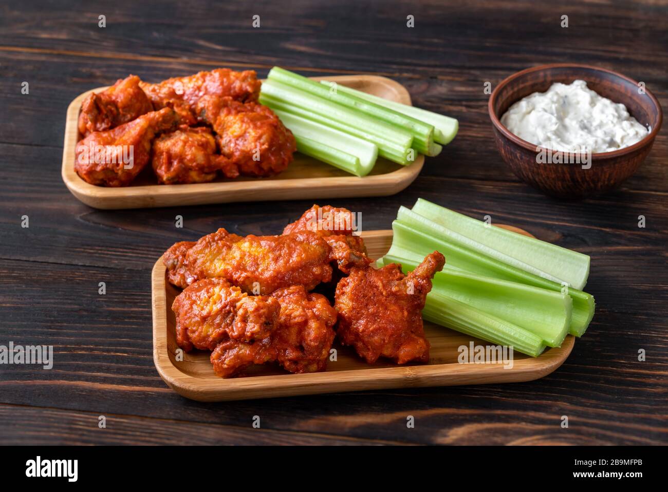Two portions of buffalo wings with fresh celery stalks and blue cheese