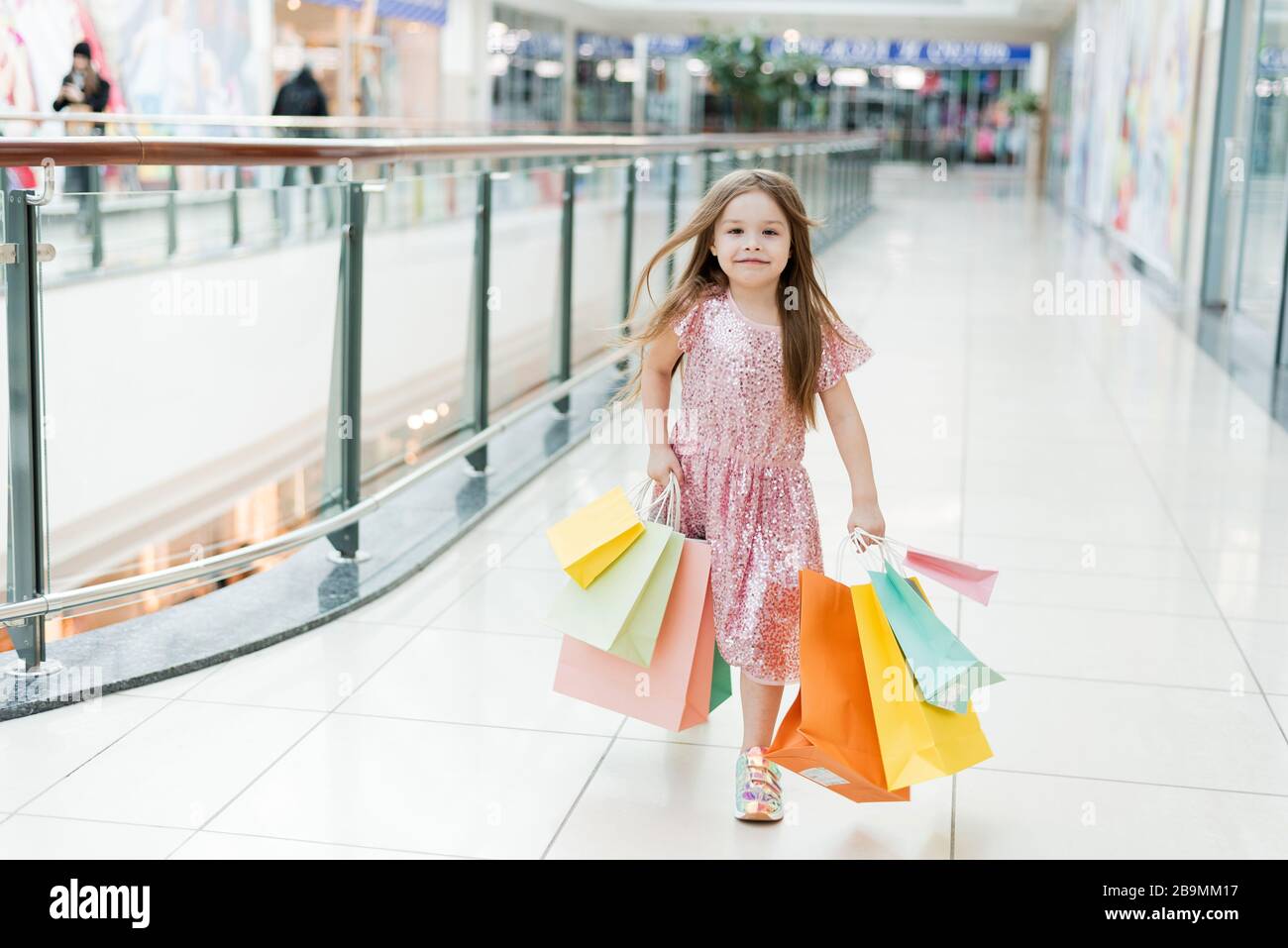 Cheerful preschool girl walking with shopping bags. Pretty smiling little girl with shopping bags posing in the shop. The concept of shopping in stores. Stock Photo