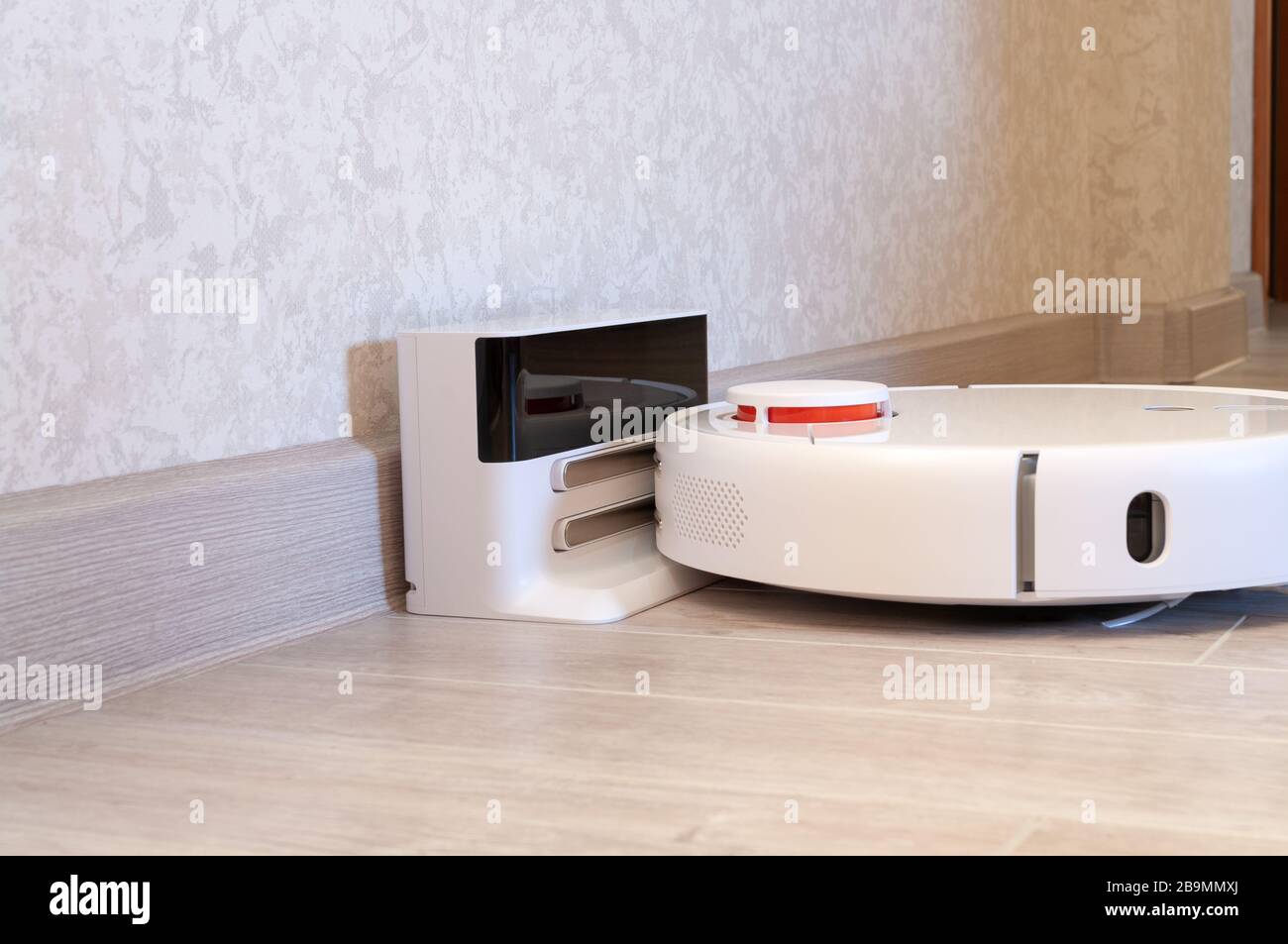 Robotic vacuum cleaner on laminate wood floor charging from base station. smart cleaning