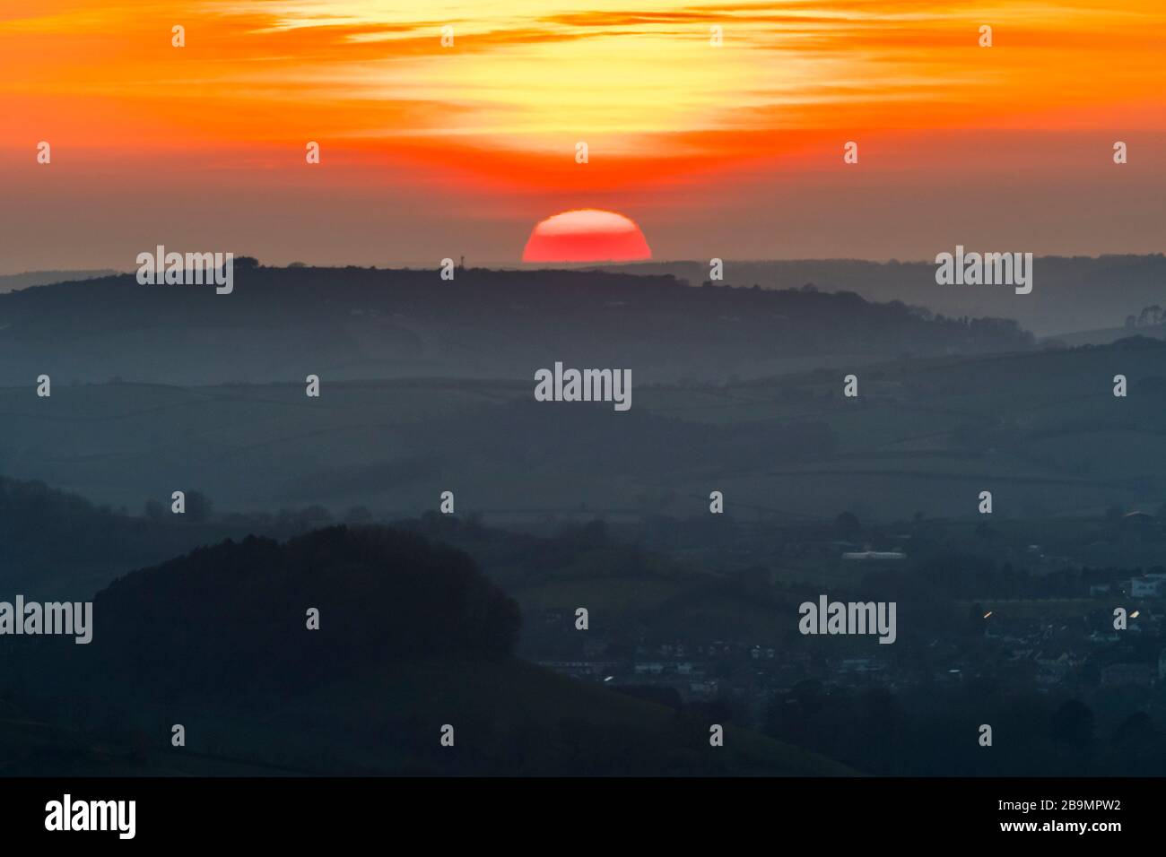 Askerswell, Dorset, UK.  24th March 2020.  UK Weather.   The sunset viewed from Eggardon Hill near Askerswell in Dorset as it sets below the hills behind Bridport to the West.  Picture Credit: Graham Hunt/Alamy Live News Stock Photo