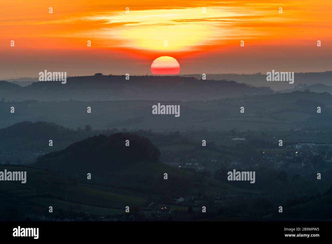 Askerswell, Dorset, UK.  24th March 2020.  UK Weather.   The sunset viewed from Eggardon Hill near Askerswell in Dorset as it sets below the hills behind Bridport to the West.  Picture Credit: Graham Hunt/Alamy Live News Stock Photo