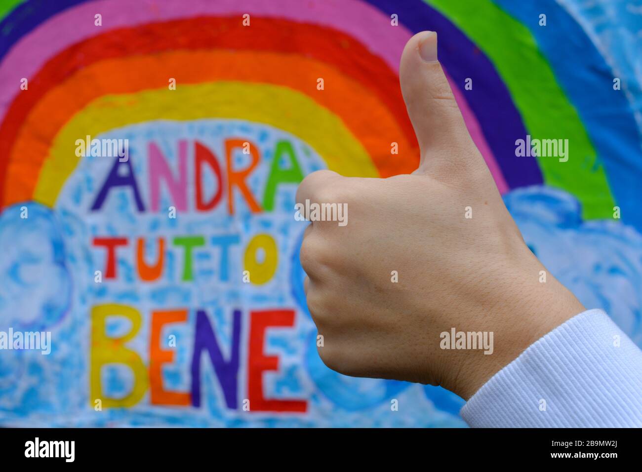 Positive message on banner translates in Everything will be alright.Close-up of a fist and sign of thumbs-up.Symbols in pandemic in Italy encouragemen Stock Photo