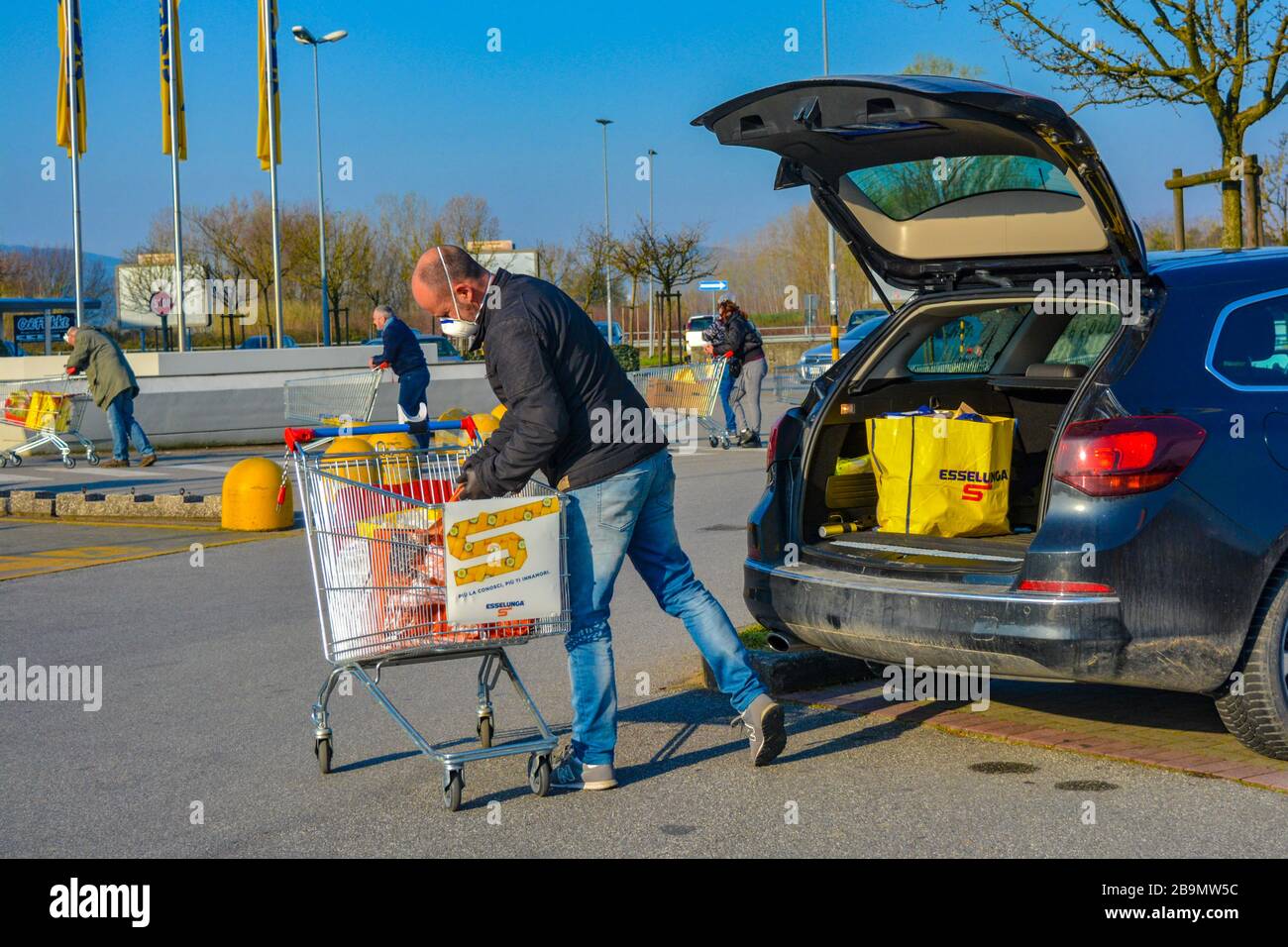 A man loading groceries in his car. Face covered with protection mask in pandemic covid19. Grocery store parking lot Stock Photo