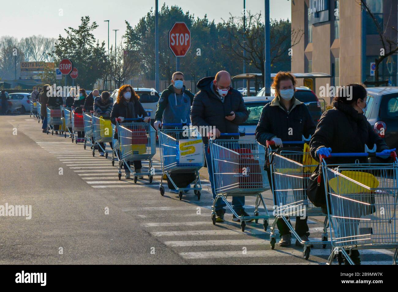 A long line of people outside the grocery store, que with shopping carts for basic needs, food and water in pandemic covid19. Customers with face mask Stock Photo