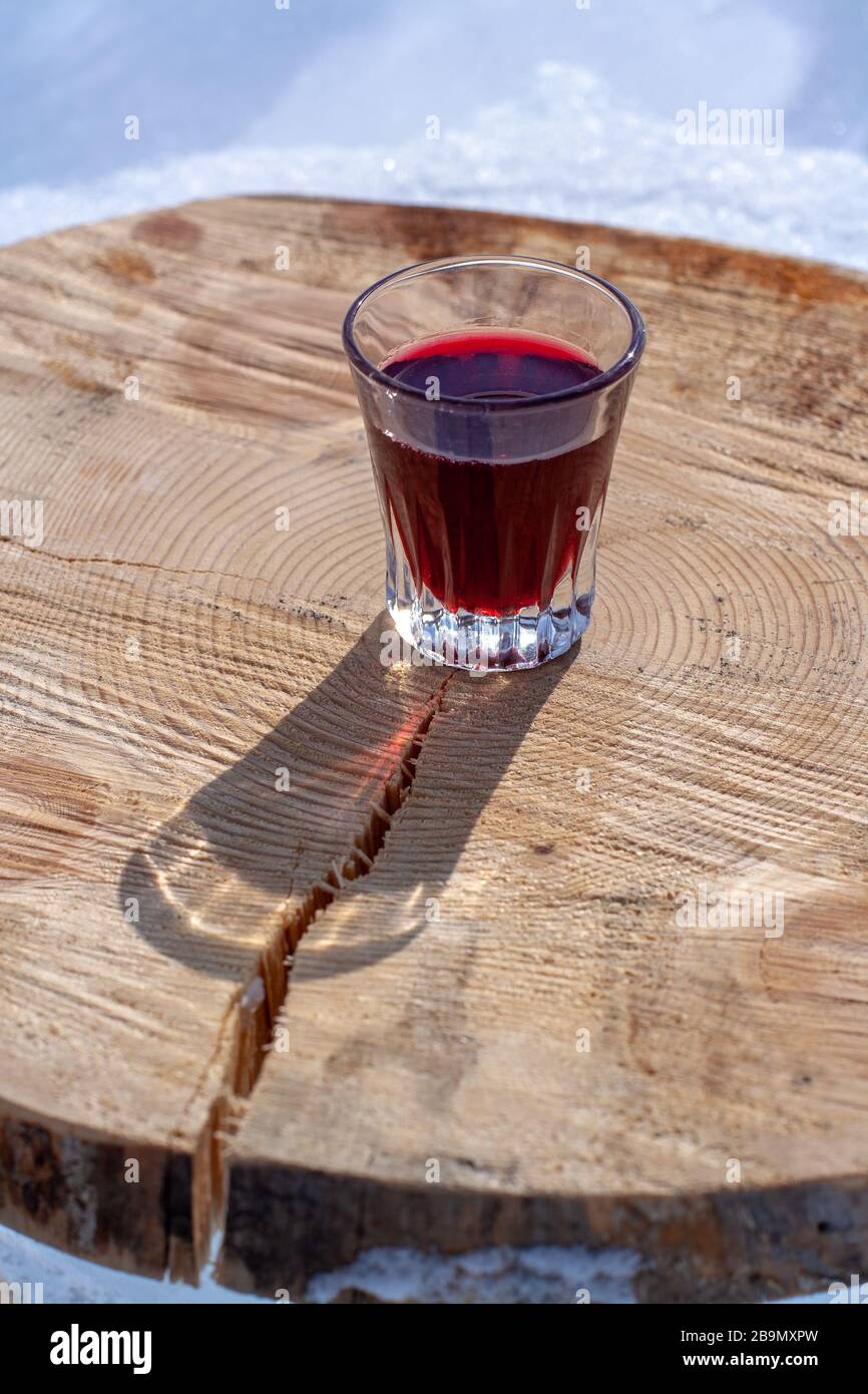 Alcoholic red tincture in a small glass stands on a cut tree stump. Liquor in a glass. Focus on the glass. Vertical. Stock Photo