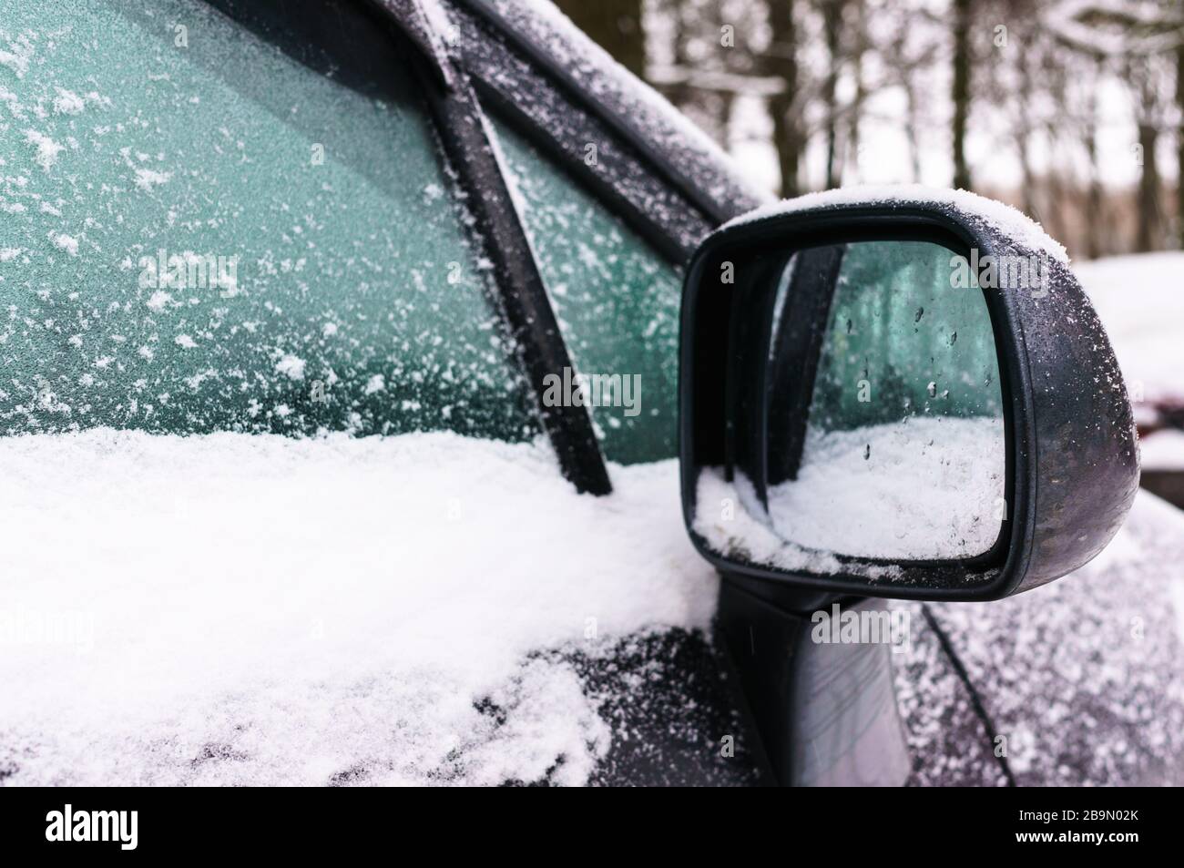 Right rear view mirror and side window of the car covered with snow. Concept of driving in winter time with snow on road. Winter season. Stock Photo