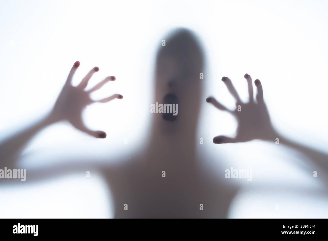 Blurred silhouette shadow of a terrorific body shape behind a white background showing head and creepy fingers. Horror concept of a visitor from out o Stock Photo