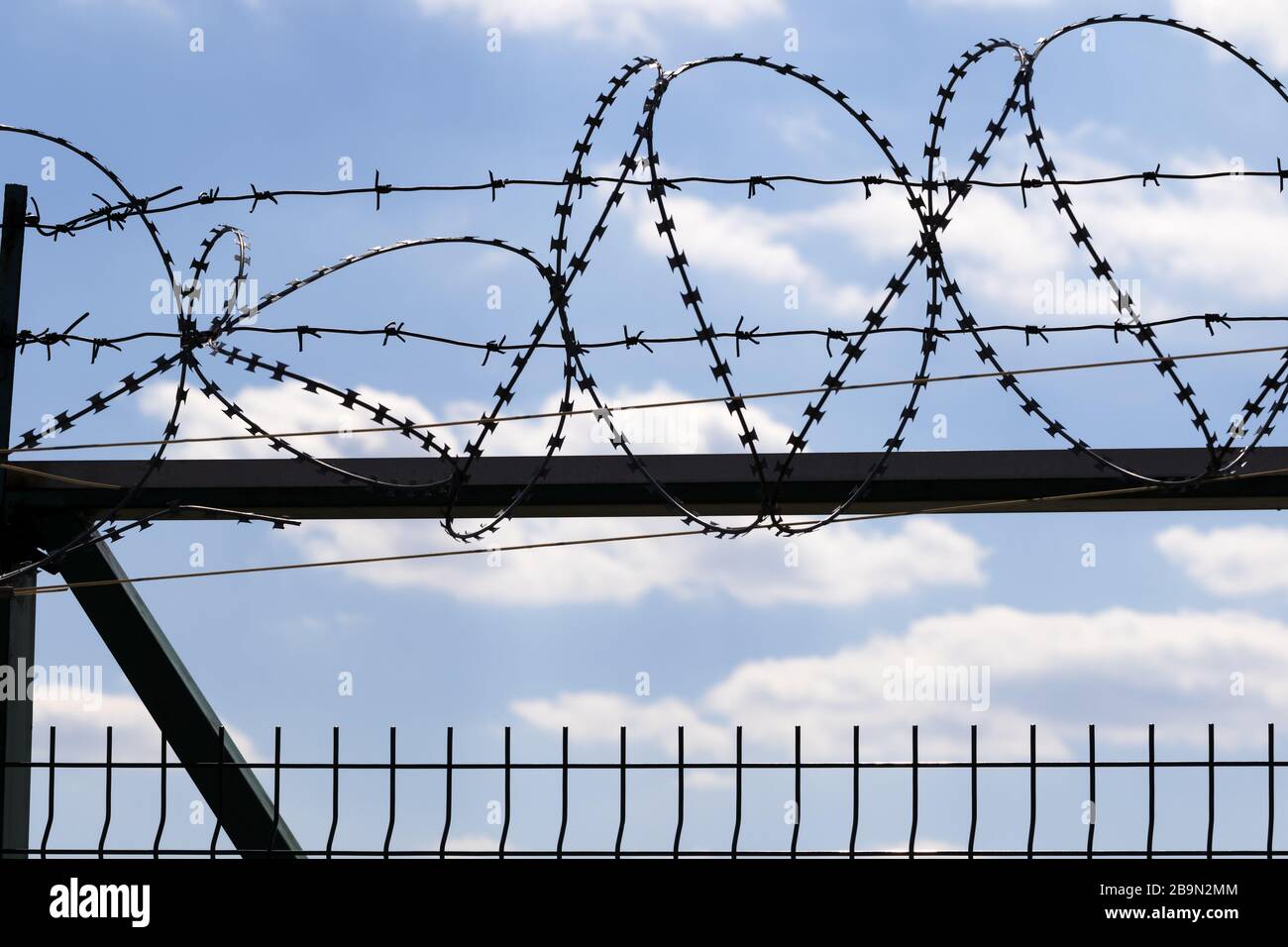 Coiled barbed wire fence and blue sky with sunlit clouds at background ...