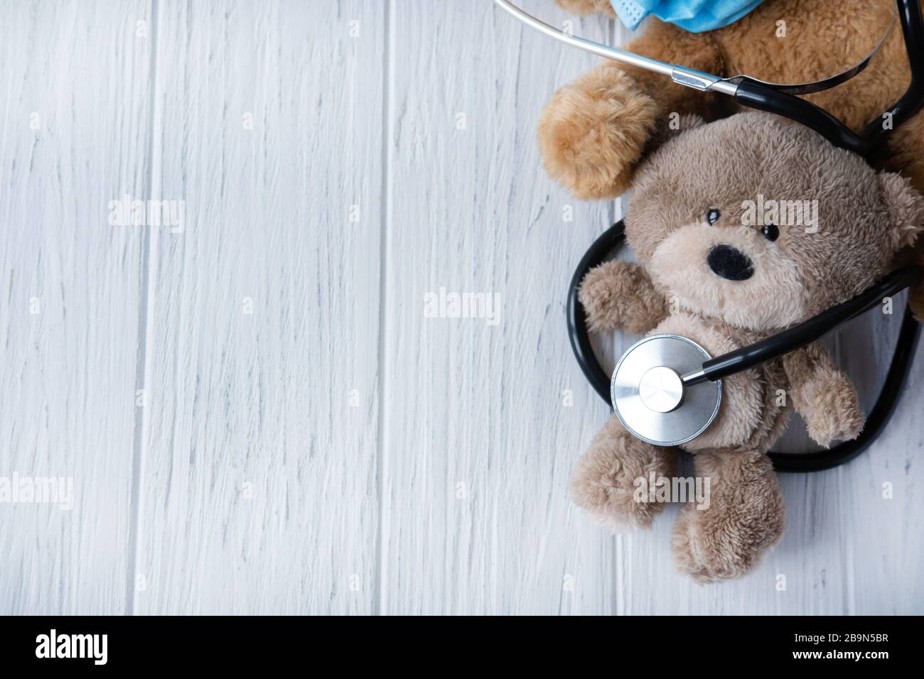 Background for banner of pediatric clinic. Treatment of childhood diseases. Toy bear with a stethoscope on a light wooden background. Stock Photo