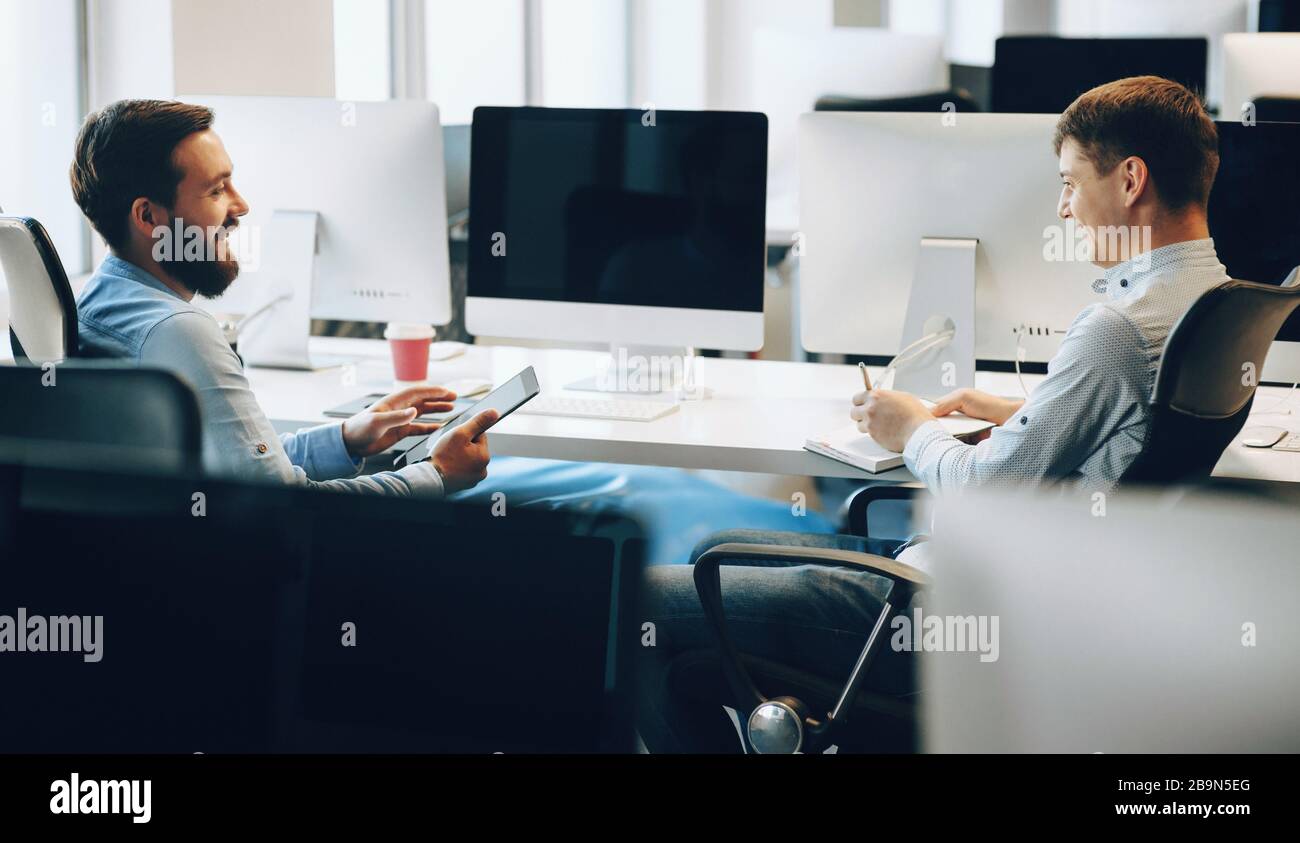 Side view photo of two caucasian men having a business discussion in their office while using a tablet Stock Photo