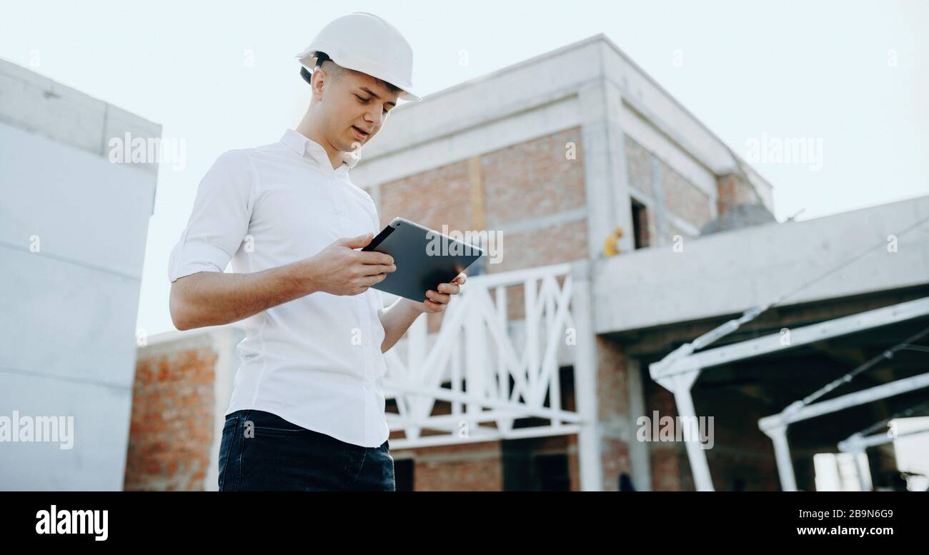 Caucasian builder looking in a tablet while making the future building plan while wearing a helmet Stock Photo