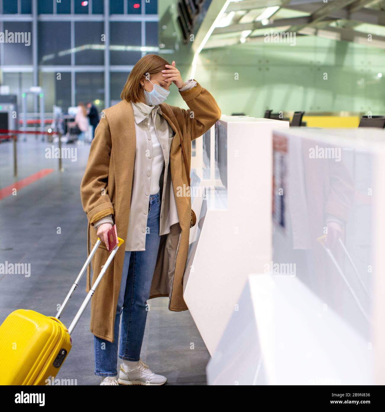 Woman with luggage upset over flight cancellation, stands at empty check-in counters at the airport terminal due to coronavirus pandemic/Covid-19 outb Stock Photo
