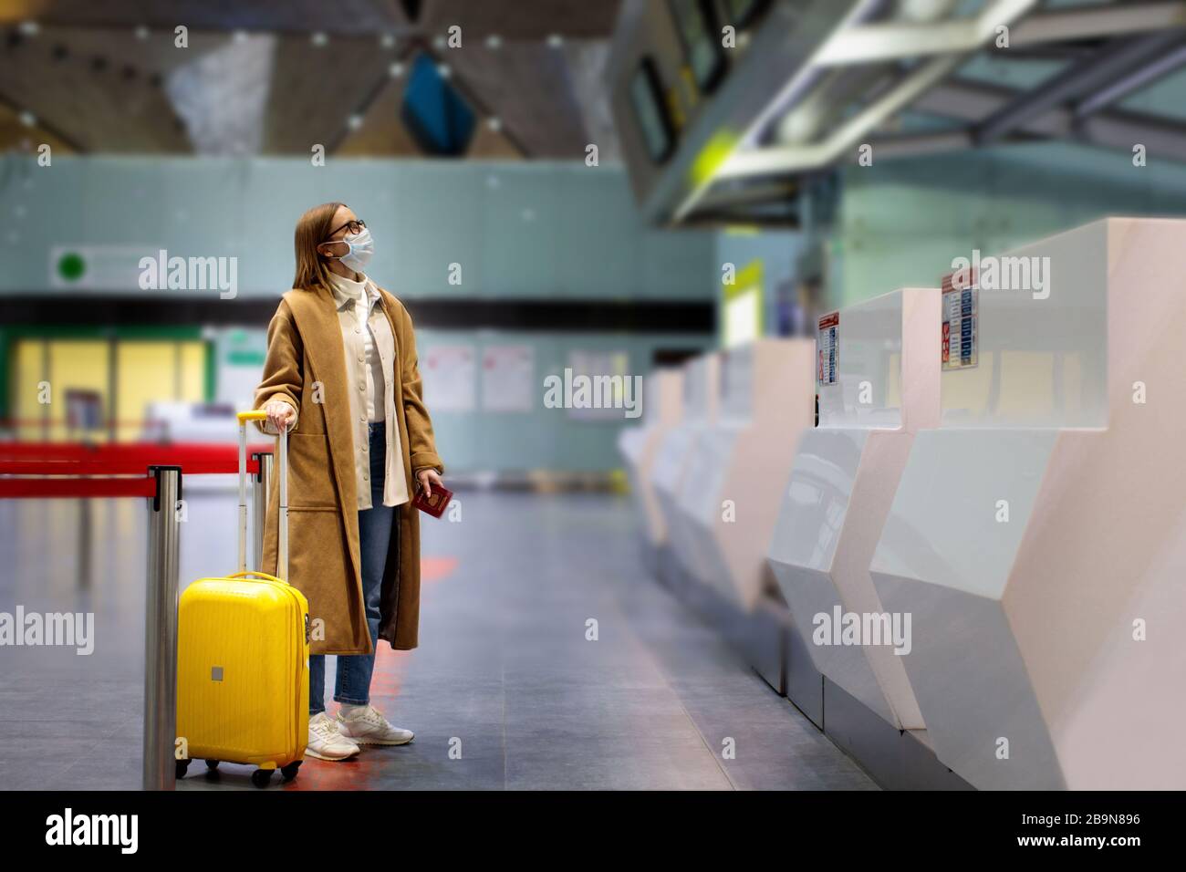 Woman with luggage stands at almost empty check-in counters at the airport terminal due to coronavirus pandemic/Covid-19 outbreak travel restrictions. Stock Photo
