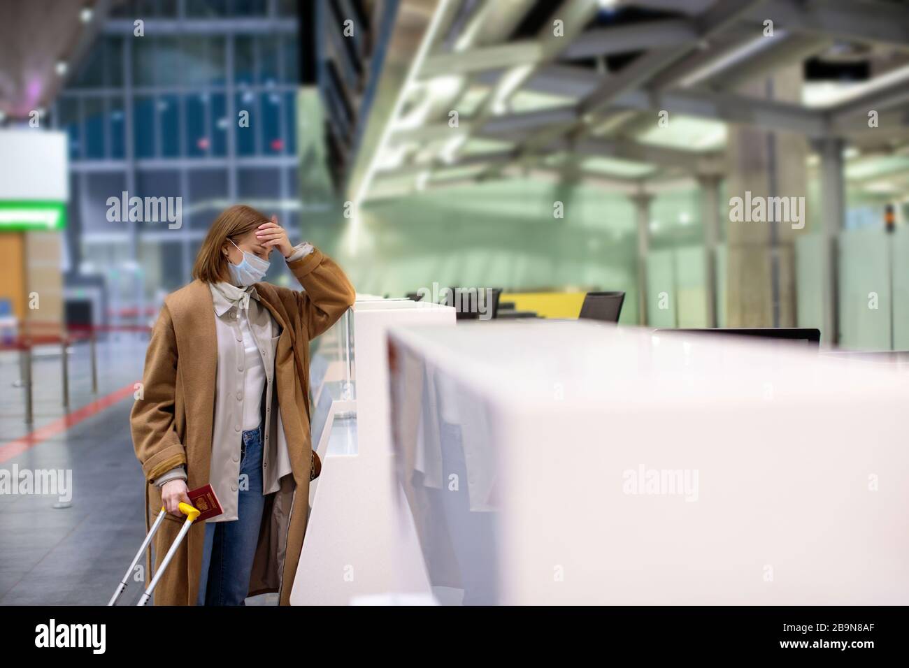 Woman with luggage upset over flight cancellation, stands at empty check-in counters at the airport terminal due to coronavirus pandemic/Covid-19 outb Stock Photo