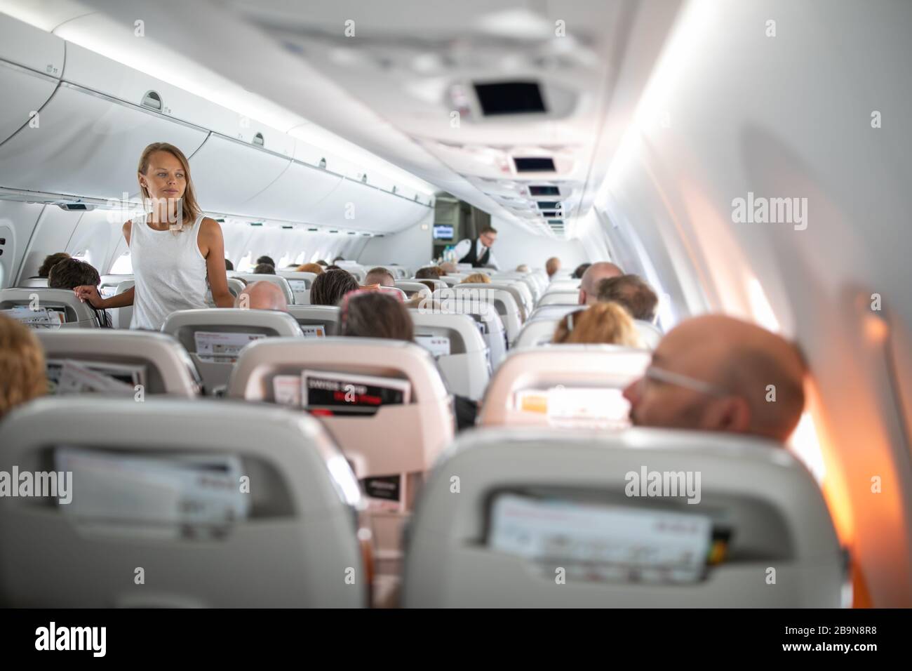Pretty, young woman aboard an airplane during a lang haul commercial flight - stretching her legs a bit, walking in the aisle Stock Photo