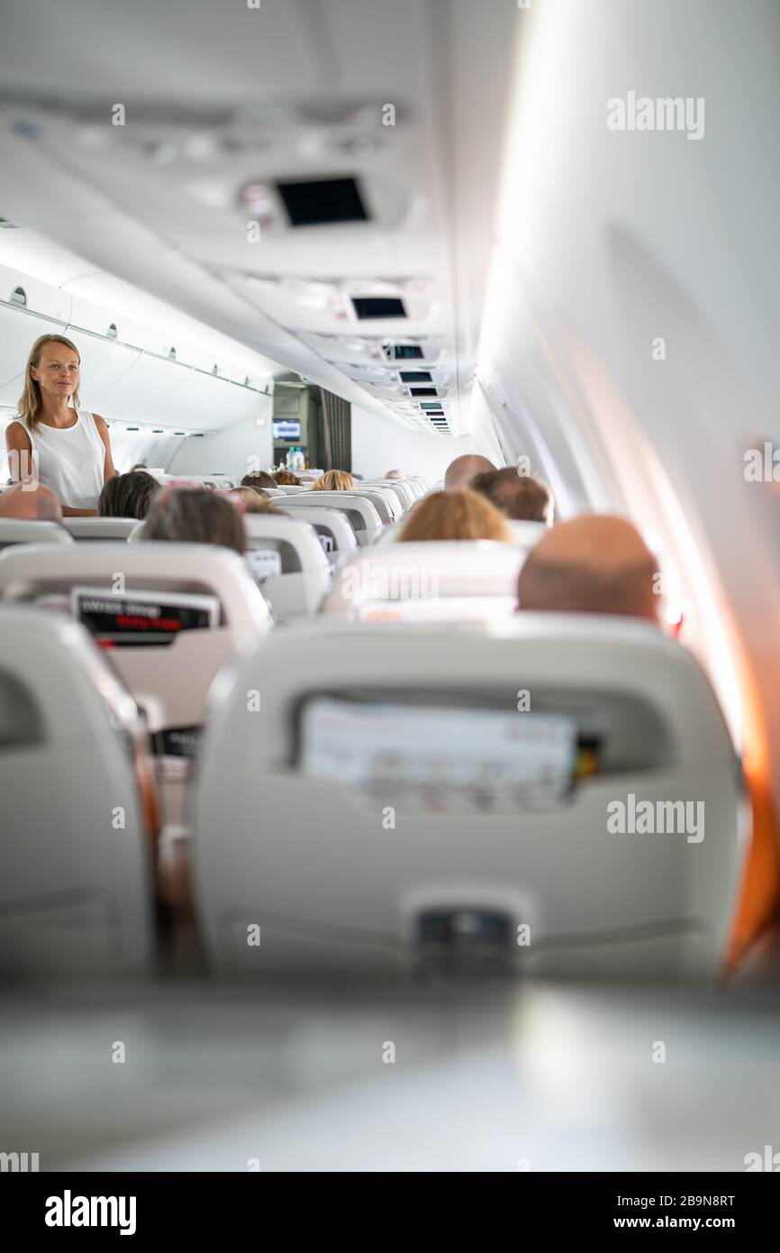 Pretty, young happy woman aboard an airplaneduring a lang haul commercial flight - stretching her legs a bit, walking in the aisle Stock Photo