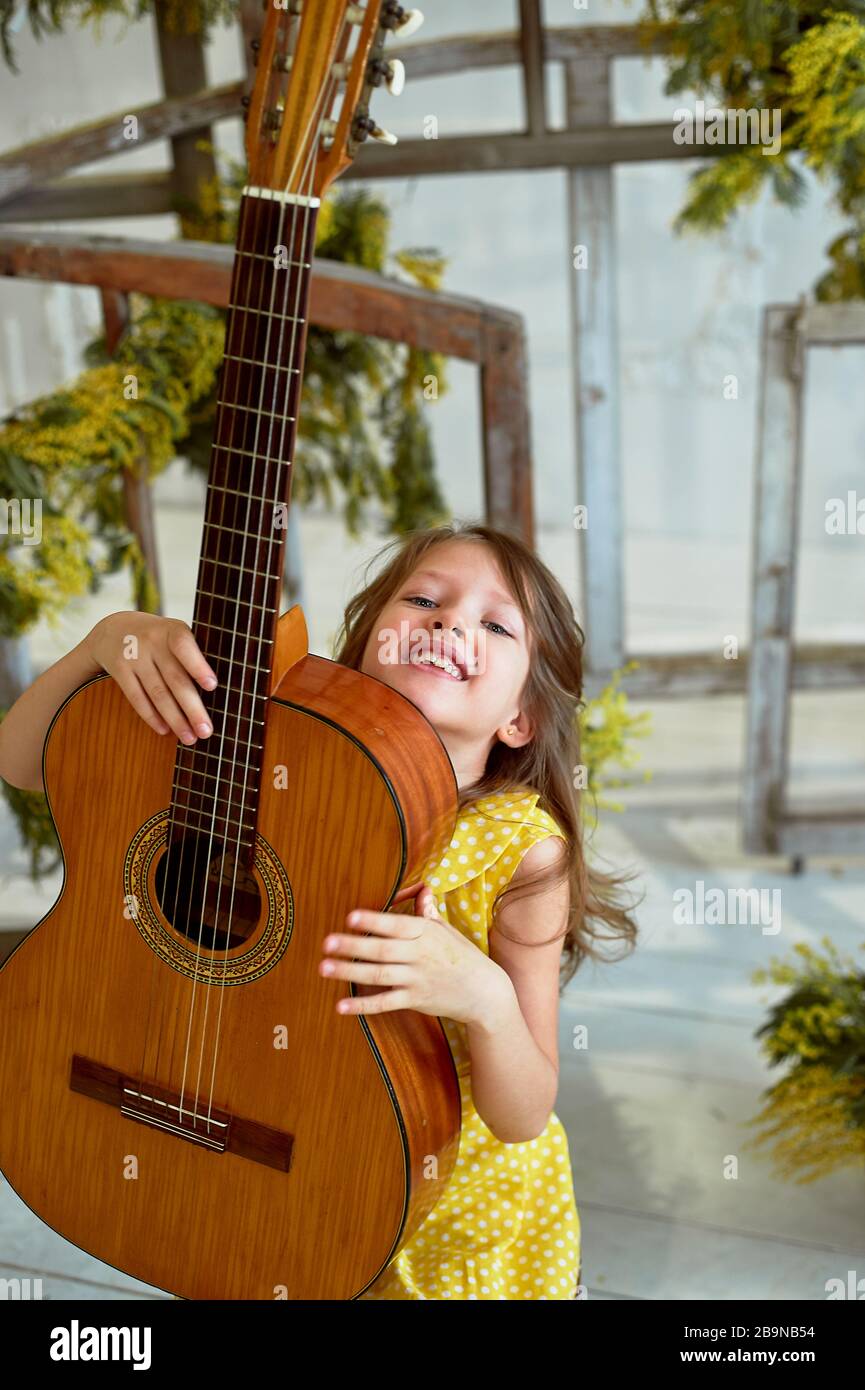Girl, 6 years old.Her hair is loose. Yellow dress, Mimosa, beautiful  interior. Laughing and holding a guitar. Music lesson Stock Photo - Alamy