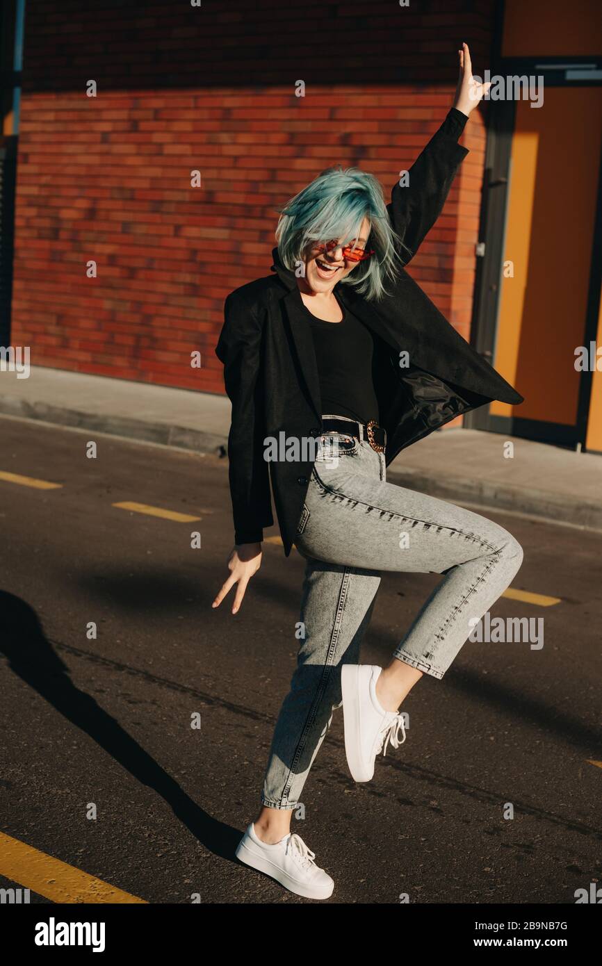 Caucasian student with blue hair dancing in the street while wearing red sunglasses Stock Photo