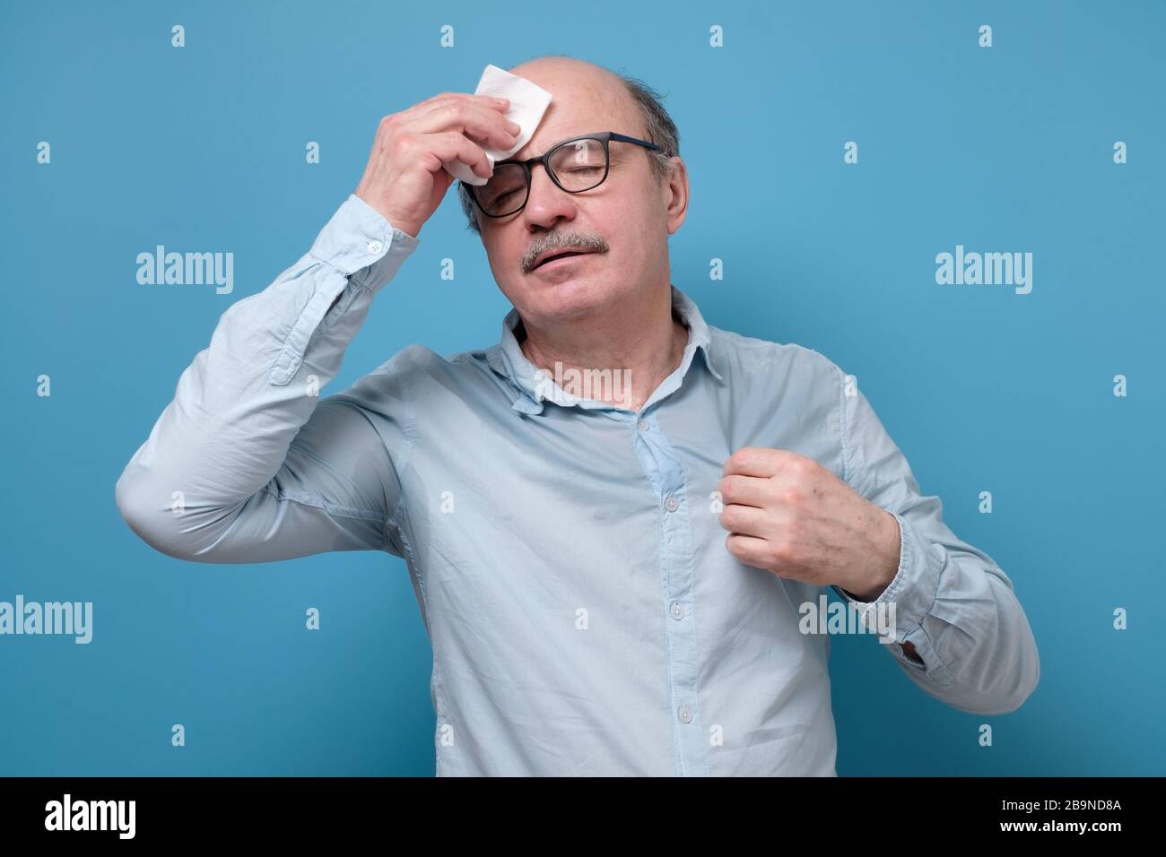 Senior employee sweating in a warm office wiping a forehead Stock Photo