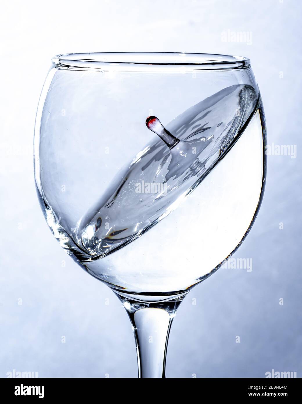 a splash of water in a glass, a falling drop. Light background. Stock Photo
