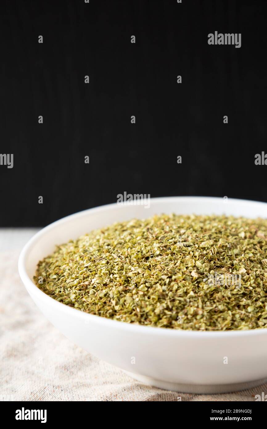 Dried Green Greek Oregano Spice in a white bowl on cloth, side view