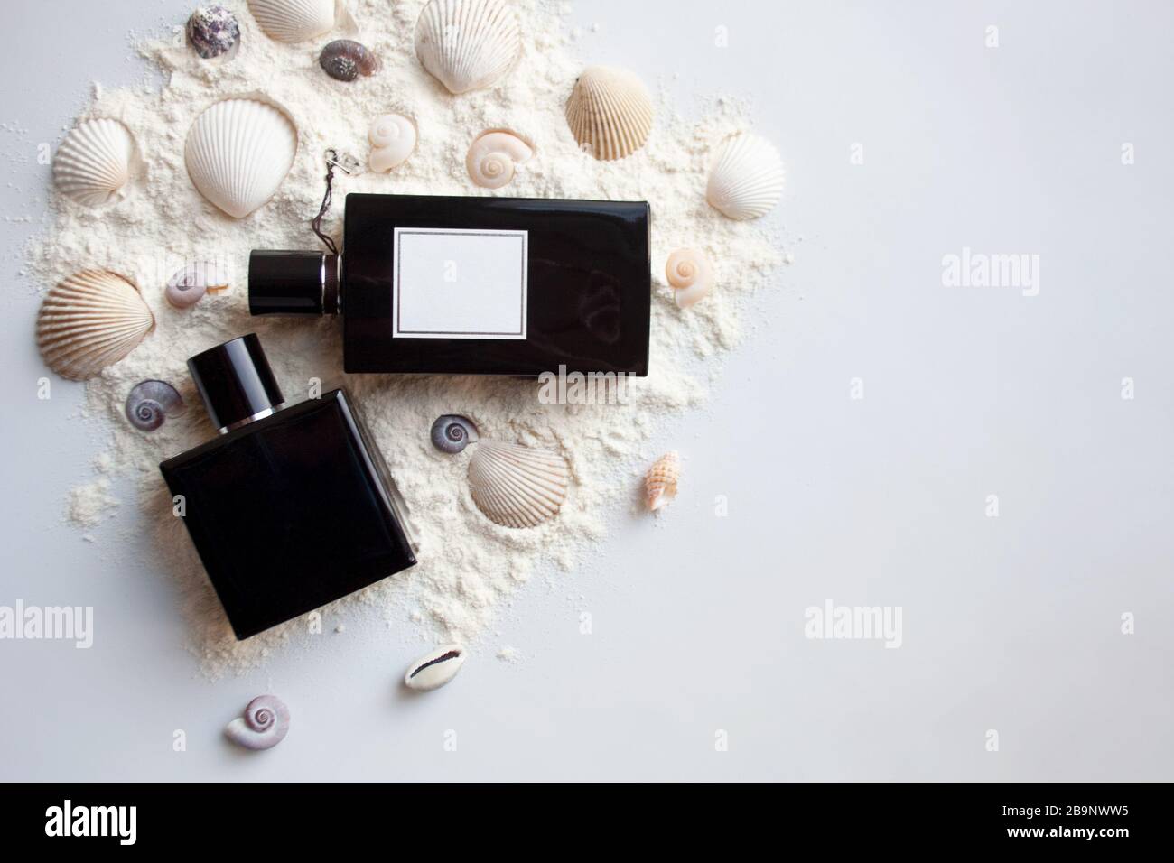 Two black glass perfume bottles on sand with sea shells and scallops Stock Photo
