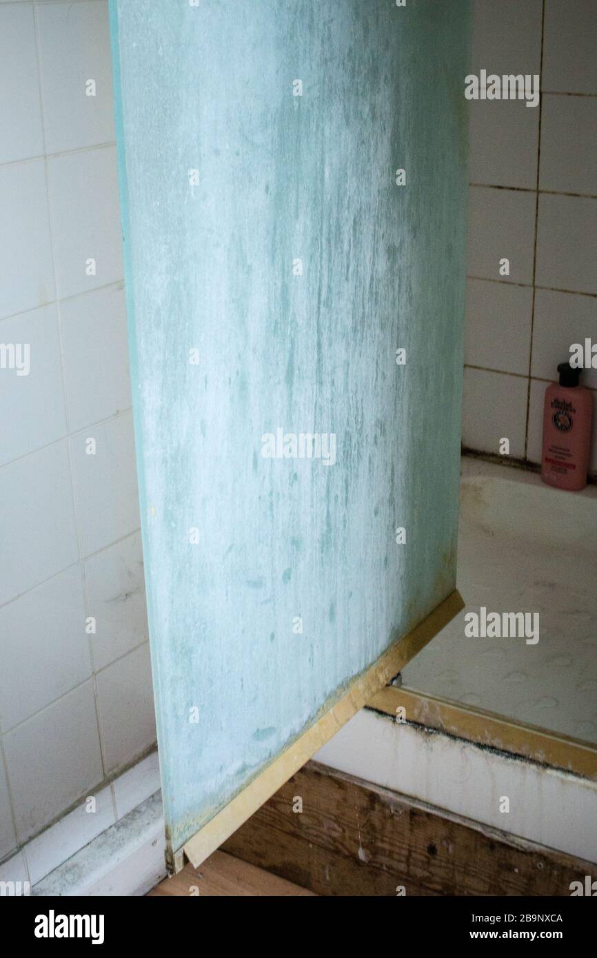 Heavily limescaled pivoting glass shower screen in dirty white tiled