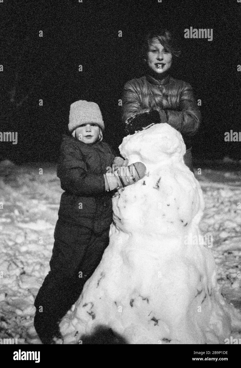Young girlfriends (both model released) complete a snowman near nightfall in Wisconsin Stock Photo