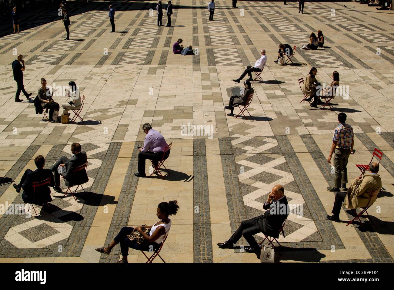 Office workers in the City of London taking breaks to enjoy the sun, mostly alone, on single chairs, facing the sun, ignoring each other. Stock Photo