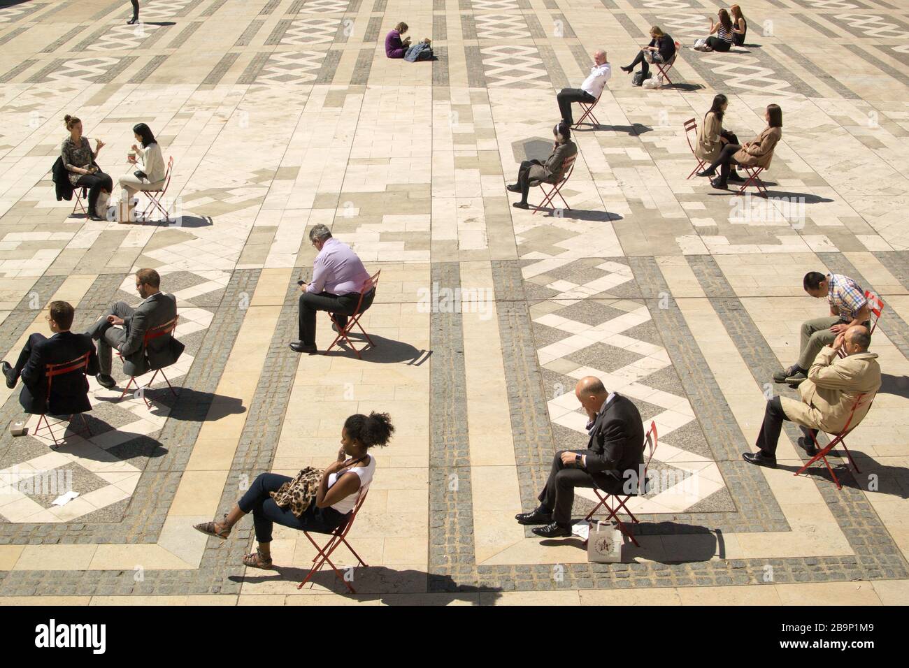 Office workers in the City of London taking breaks to enjoy the sun, mostly alone, on single chairs, facing the sun, ignoring each other. Stock Photo