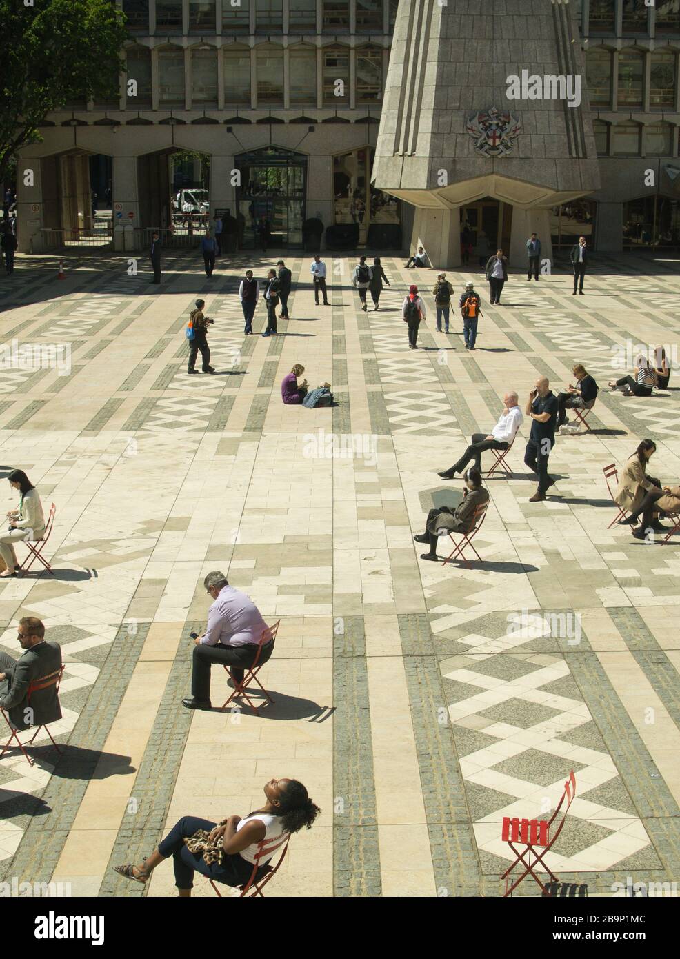 Office workers in the City of London taking breaks to enjoy the sun, mostly alone, on single chairs, facing the sun, ignoring each other. Stock Photo