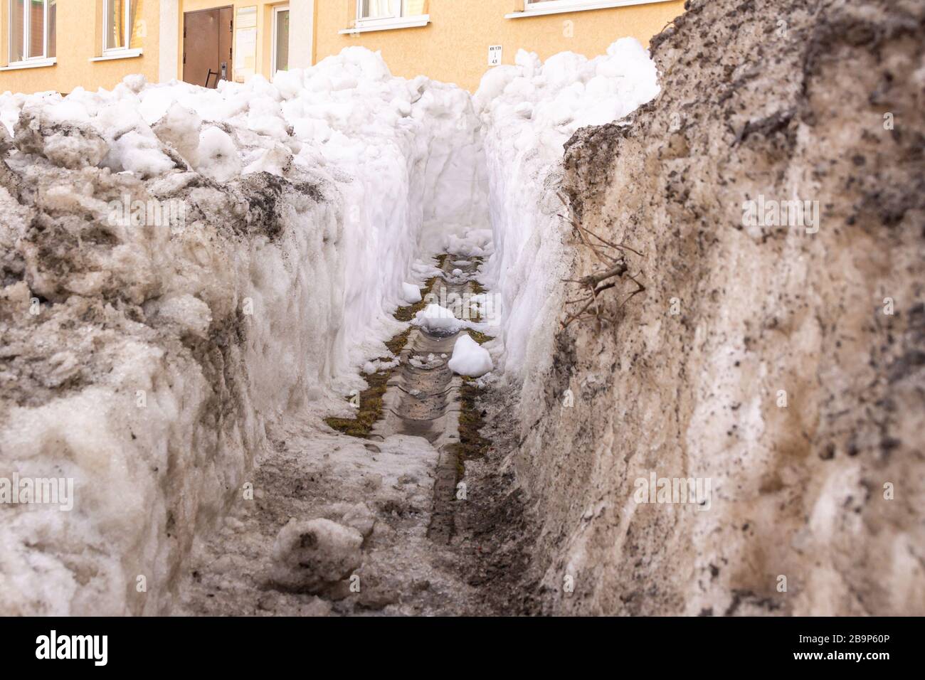 cleaning the gutter from wet and darkened snow in the spring to divert the flow of meltwater from the building Stock Photo