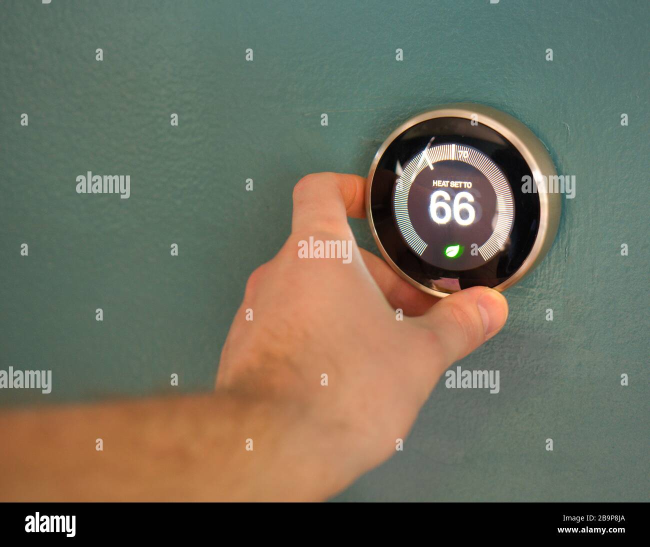 Hand adjusting temperature on electric thermostat. Temp set at 66