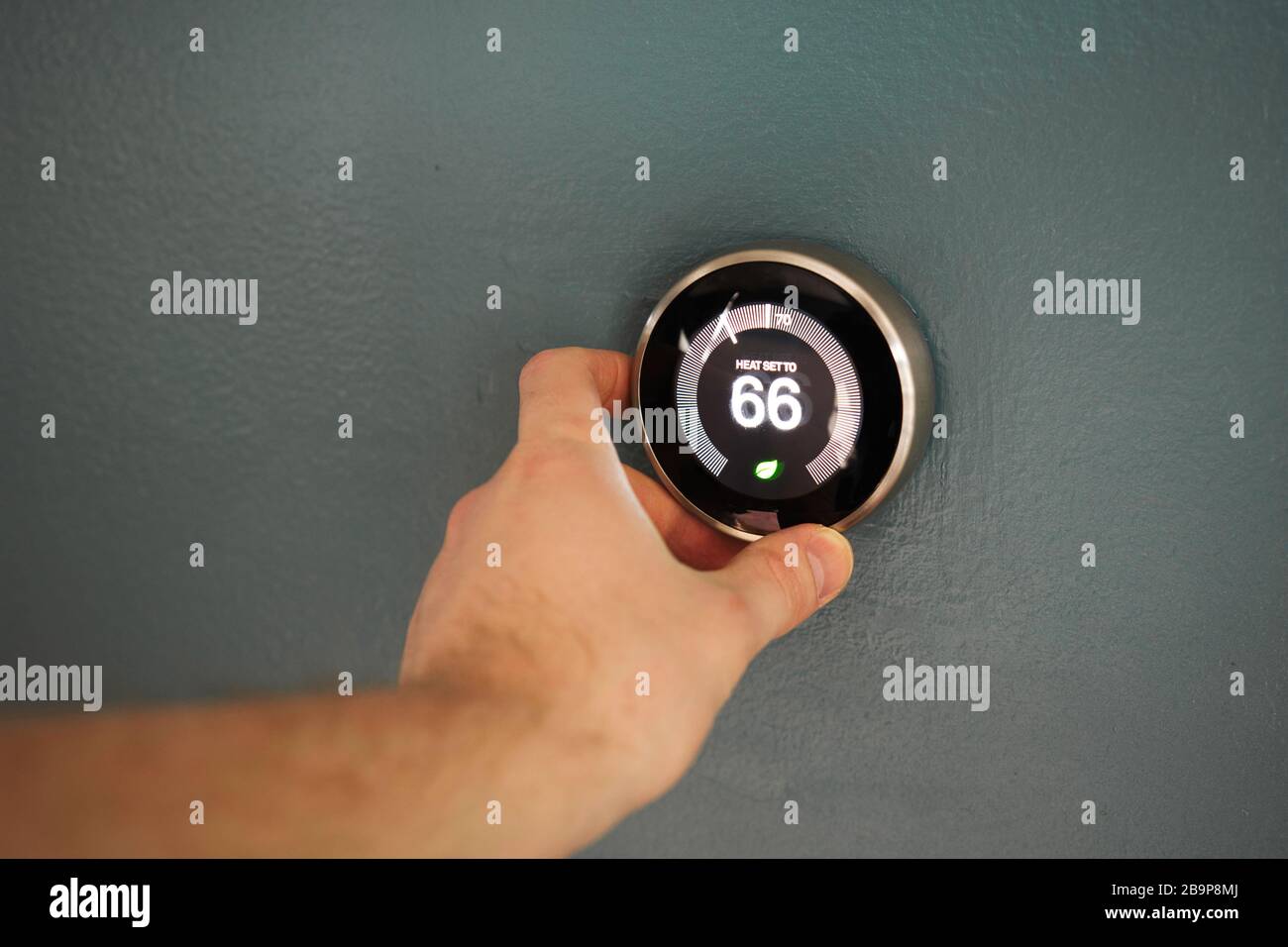 Hand adjusting temperature on electric thermostat. Temp set at 66