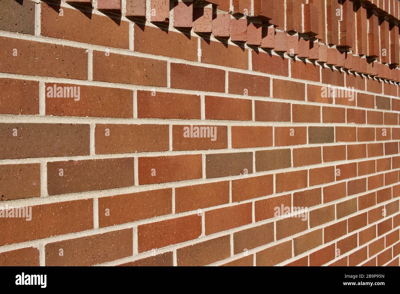 Protruding bricks in geometric shapes decorate the top of this traditional reddish brown brick wall texture background, with sunlight cast shadows Stock Photo