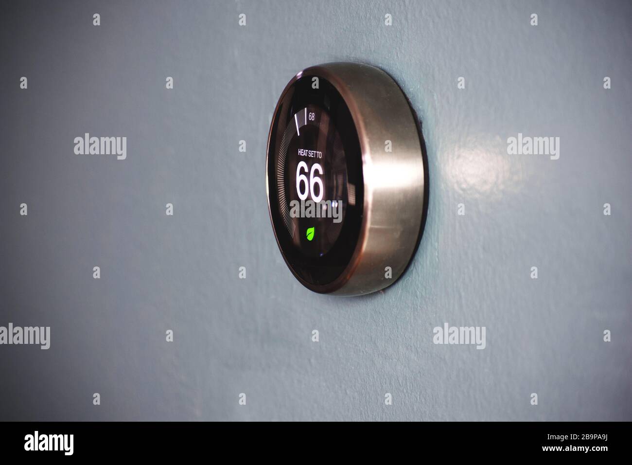 Thermostat isolated on light blue wall. Smart home tech to save money and energy. Stock Photo