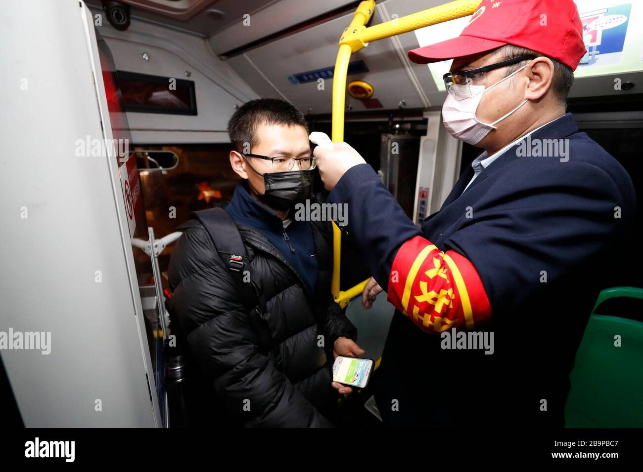 (200325) -- WUHAN, March 25, 2020 (Xinhua) -- A staff checks a passenger's body temperature on a bus in Wuhan, central China's Hubei Province, March 25, 2020. Wuhan, the once hardest-hit city in central China's Hubei Province during the COVID-19 outbreak, resumed a total of 117 bus routes starting Wednesday, around 30 percent of the city's total bus transport capacity, the municipal transport bureau said. According to a spokesperson of the bureau, passengers must wear masks, register with their names and scan a QR code, and take a temperature check before taking buses and subways. (Xinhua/Sh Stock Photo