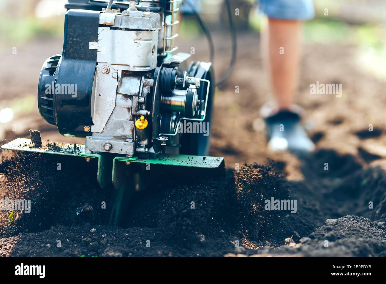 close up photo of young farmer gardener cultivate ground soil rototiller , tiller tractor, cutivator, miiling machine, prepare for planting crop Stock Photo