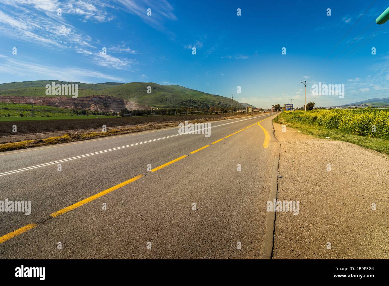 Asphalt road painted in white and yellow surrounded by green field and ...