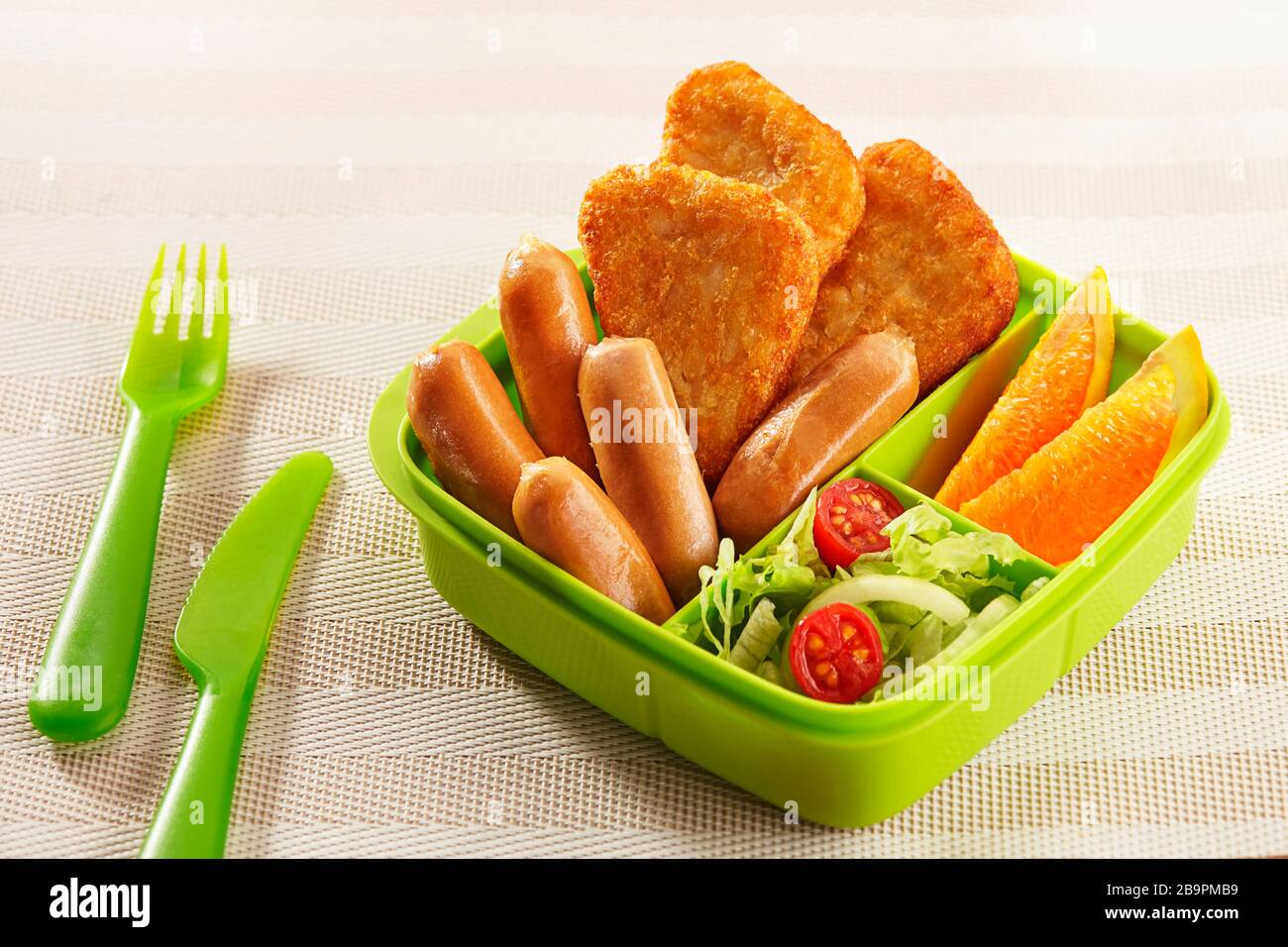 Packed lunch boxes filled with hash brown, cocktail sausages, orange fruits and salads, ready to be taken for activities Stock Photo